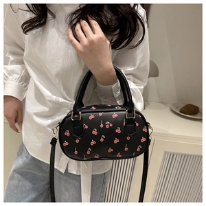Detail of black cylindrical bag featuring red cherry print and adjustable shoulder strap