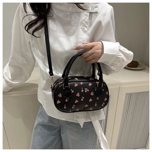 Detail of black faux leather bag featuring cherry print and adjustable shoulder strap