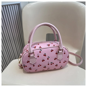 Detail of pink PU leather handbag with red cherry print on a white chair surface