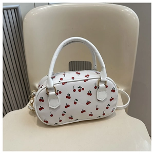 Close-up of white Boston bag featuring red cherry prints and gold metal hardware detail