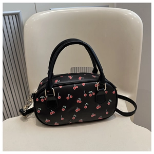 Detailed view of the black Boston bag featuring red cherry prints and golden hardware