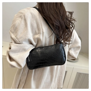 Close-up of black crocodile texture on a baguette shoulder bag with a fashion tag