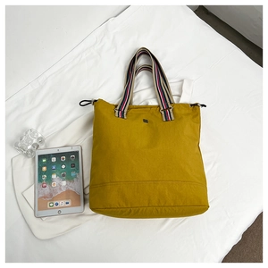 Detail einer gelben Stofftasche mit lebhaften, farbig gestreiften Webbandgriffen