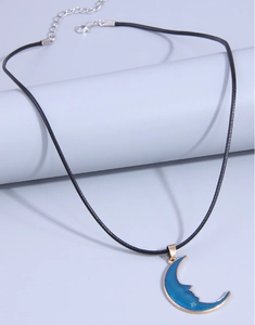 Macro detail of crescent moon pendant with blue enamel and gold star on black cord
