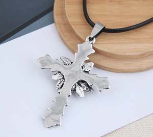 Macro detail of silver vintage cross pendant with floral engraving on a black cord necklace