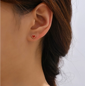 Close-up of a red heart stud earring with rose gold finish on a model's ear