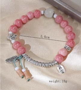 Macro shot of pink marble beads bracelet with silver feather and prosperity tag detail