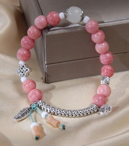 Detailed shot of pink beaded bracelet with silver feather charm and Lucky tag