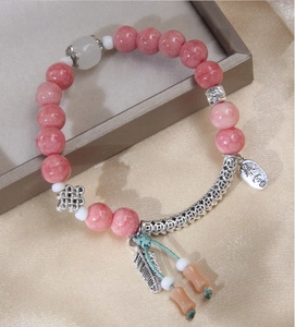 Detail of pink beaded bracelet with silver feather pendant and peace charm on satin