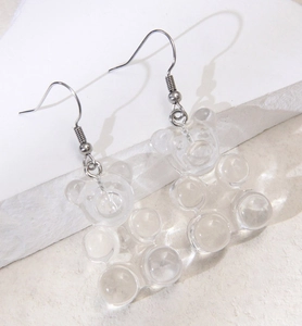 Detailed view of clear resin bear earrings with silver hooks on white stone texture