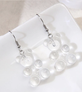 Close-up of transparent gummy bear earrings in white ceramic dish, clear resin design