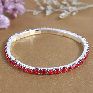 Elastic silver bracelet with single row of red rhinestones on gold fabric background
