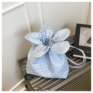 Detail of blue gingham drawstring bucket bag with petal-shaped opening on a suitcase