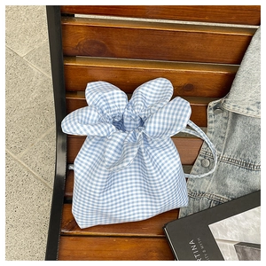 Detail of blue gingham drawstring bucket bag with floral petal edge on a wooden bench