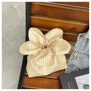 Detail of yellow gingham canvas bucket bag with petal-shaped drawstring closure on wooden bench