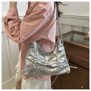 Detail der silbernen Metallic-Schultertasche mit Faltenstruktur und Schleifen am Modell