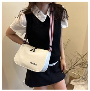 Close-up of a white canvas crossbody bag featuring a stylish tricolor woven shoulder strap