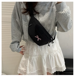 Detail view of black nylon crossbody bag featuring a pink bow and adjustable strap