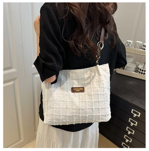 Detail of white tote bag with woven texture, brown leather tag and strap on a model