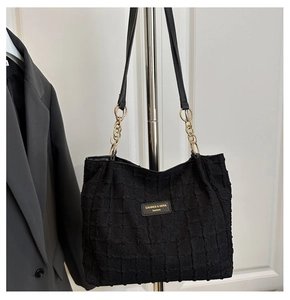 Close-up of black textured tote bag featuring gold chain strap and brand emblem