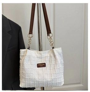 Close-up of white tweed woven tote bag with chain strap and leather brand label