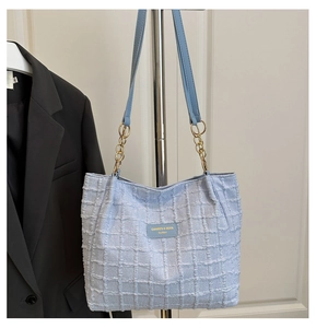 Detail of light blue tweed tote bag with gold chain strap and embossed leather logo tag