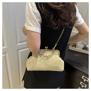 Beige straw woven shell clutch shown crossbody on a model in a minimal room setting