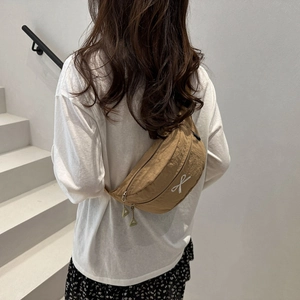 Sac bandoulière kaki mignon avec broderie nœud porté par un mannequin en décor minimaliste