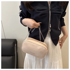 Detail of a beige mini square crossbody bag with chain strap and top zipper closure