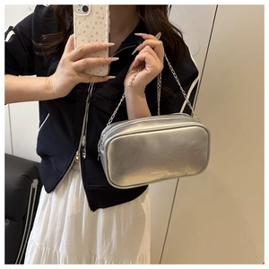 Silver metallic makeup bag with dual zippers and chain strap shown in use
