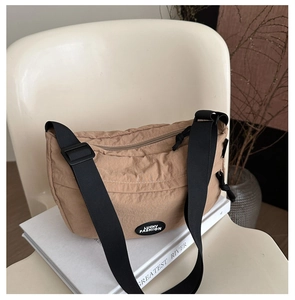 Close-up of khaki nylon dumpling bag with black strap and Lucky Fashion logo on a chair