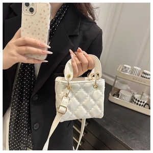 Close-up of white quilted mini bag with gold hardware worn with a black blazer
