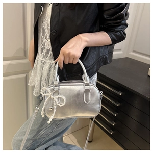 Detail der silbernen Metallic-Handtasche mit Perlen-Schleifen-Anhänger und Schultergurt