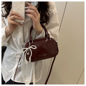 Close-up of wine red patent leather handbag with pearl bow charm and fashion lettering