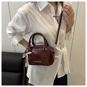 Détail du sac polochon en cuir bordeaux avec breloque nœud perlé et bandoulière
