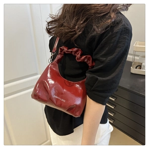 Detail view of burgundy patent leather bag with ruched handle and fashion text logo