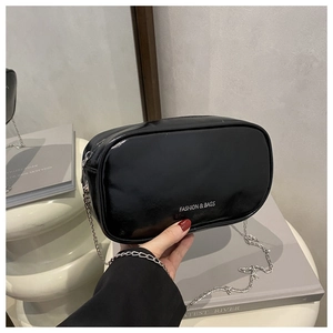 Detail of black glossy patent leather crossbody bag with silver chain on white podium