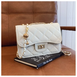 Detail of white quilted crossbody bag with golden chain and decorative gold ball charm