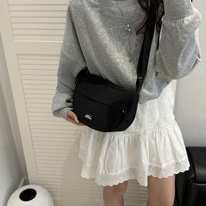 Minimalist black nylon crossbody bag with Lucky Fashion patch on grey sweater model