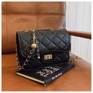 Close-up of black quilted shoulder bag with gold sphere charm and chain strap detail