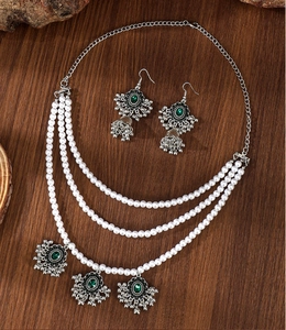 Detail of vintage multi-layer pearl necklace and bell earrings with green gemstones