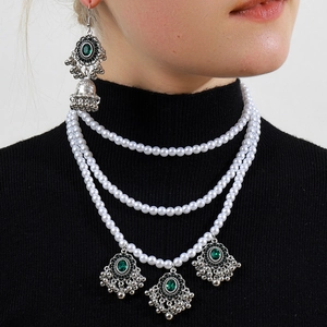 Macro detail of multi-layer pearl necklace with green gemstones on black turtleneck