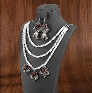 Detail of layered pearl necklace and silver jhumka earrings with red crystal accents