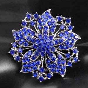 Elegant silver flower brooch with sparkling deep blue crystals on black background