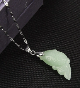 Vue macro d'un pendentif poisson en jade vert avec une chaîne argentée sur noir
