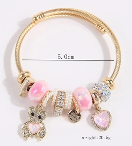 Close-up of golden beaded bracelet featuring a rhinestone bear and pink heart charms