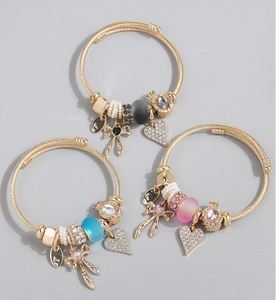 Dettaglio di ciondoli a cuore e fiocco su bracciali in filo d'oro con perline