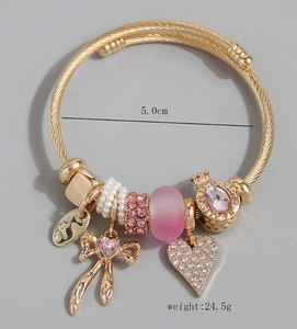 Dettaglio del bracciale dorato a treccia con ciondoli cuore rosa, fiocco e corone