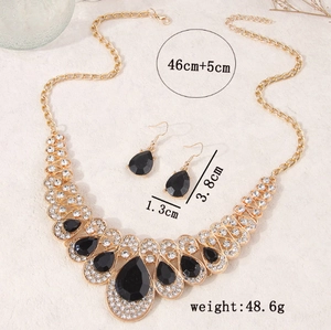 Detailed shot of golden necklace and teardrop black gemstone earrings set on stone