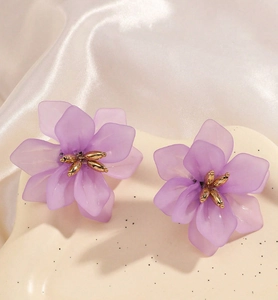 Macro shot of purple petal flower stud earrings with golden stamens on white silk fabric